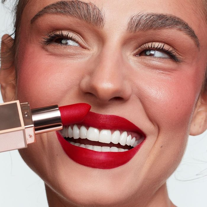 A close-up shot of a cheerful model applying red lipstick.
