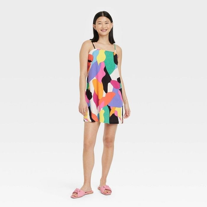 A model wearing a dress featuring a bold pattern of pink, green, yellow, orange, black, white, and purple, matched with pink shoes
