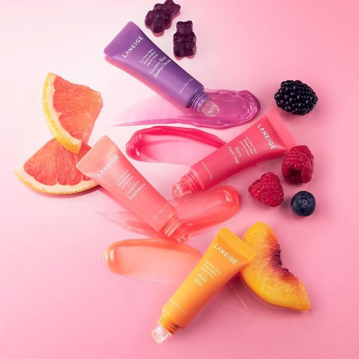 An assortment of Laneige lip sleeping masks displayed with fruit slices and berries on a pink backdrop, evoking flavor inspiration for your skincare shopping needs