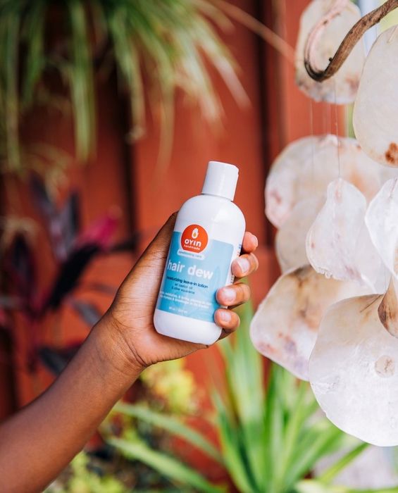 A hand holding the bottle of Oyin Handmade’s Hair Dew Leave-In Lotion.