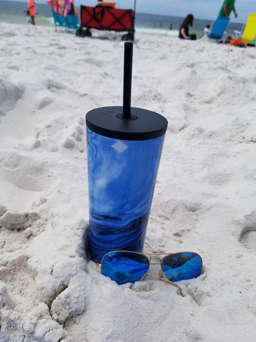The iced coffee cup placed on the sandy beach, with the reviewer’s perspective
