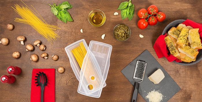 The rectangular-shaped cooker, featuring spaghetti inside, along with a lid that includes a strainer and two measuring holes for precise pasta portions.