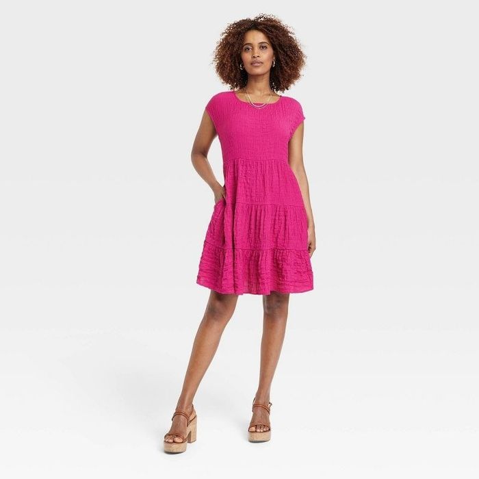 A model is showcasing a vibrant pink dress paired with brown shoes.