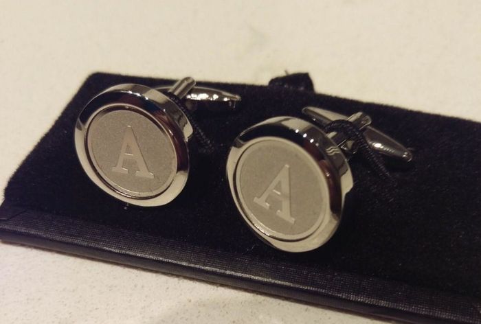 A reviewer’s pair of silver-toned cufflinks featuring the letter A, with a rounded design and an engraved border