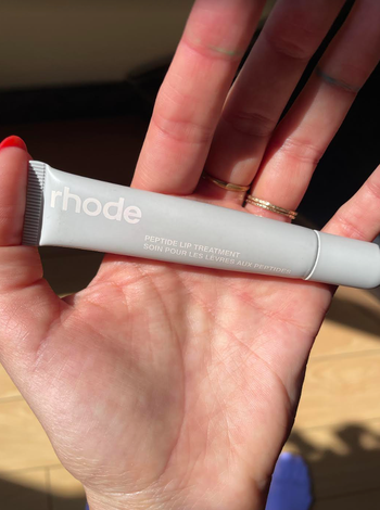 A hand gently holding a tube of lip treatment.