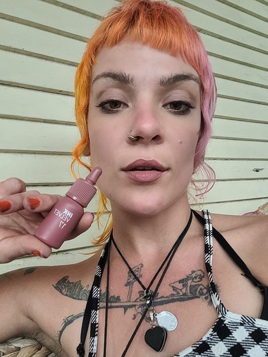 Reviewer holding the pink bottle of Velvet Lip Tint while wearing it on their lips.