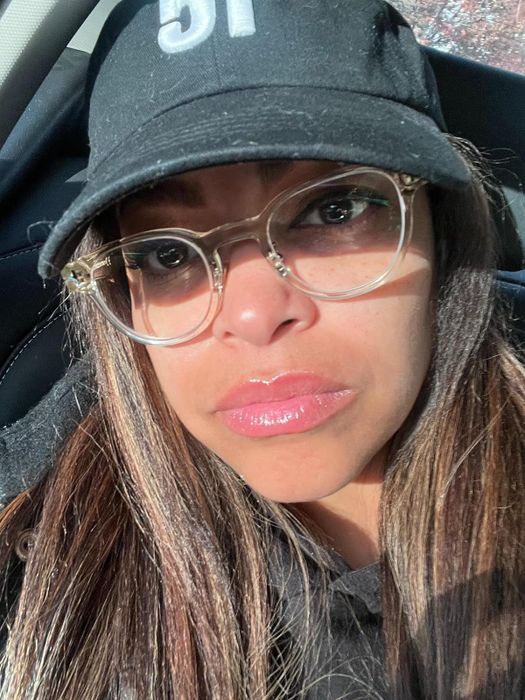 A person wearing a cap and clear glasses takes a close-up selfie inside a car