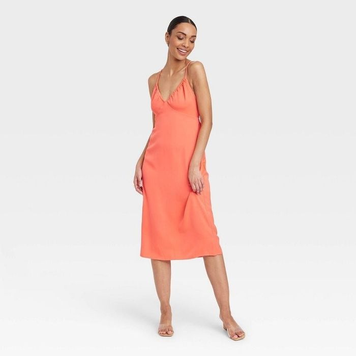 A model in an orange midi dress paired with clear shoes.