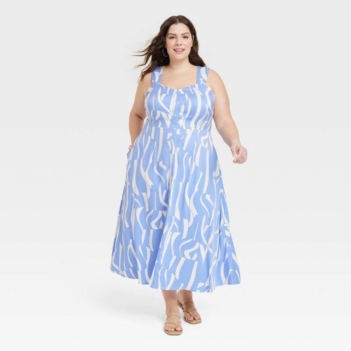 A model is shown wearing a blue and white dress paired with nude sandals.