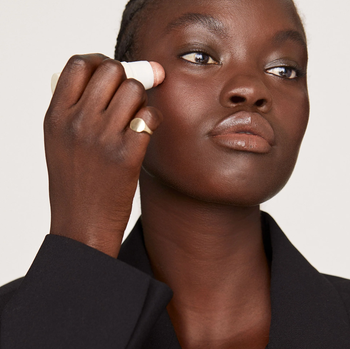 A model applies the highlighting balm to their face