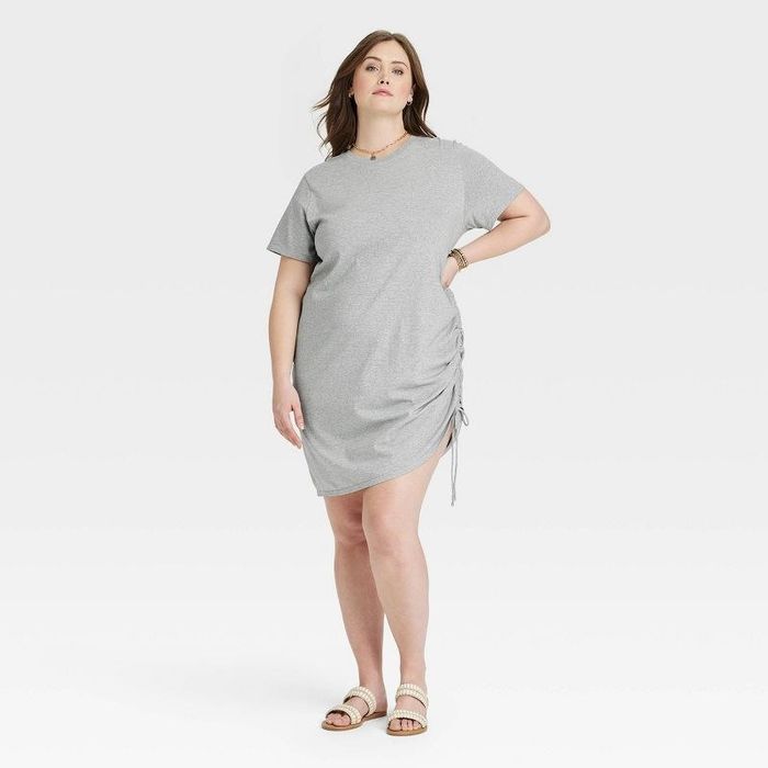 A model is wearing a grey T-shirt dress paired with white shoes.