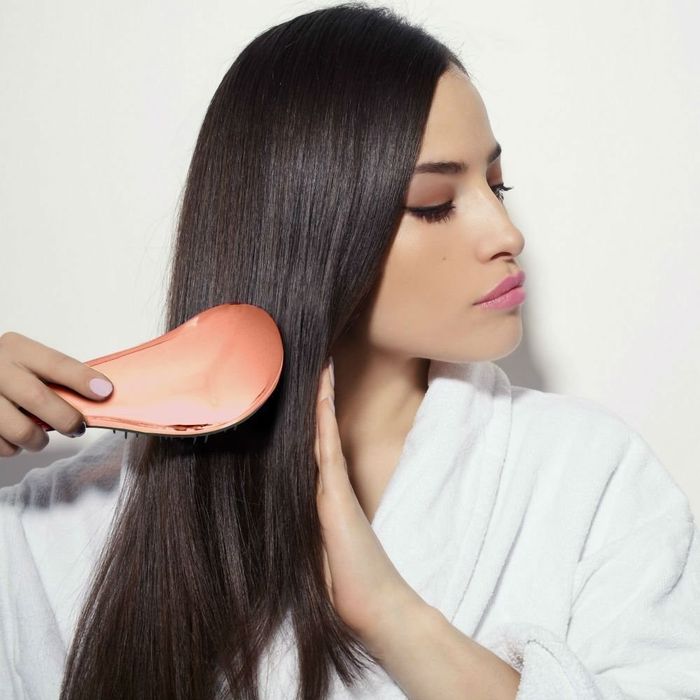 A model demonstrating the use of a rose gold hair brush to style her hair.
