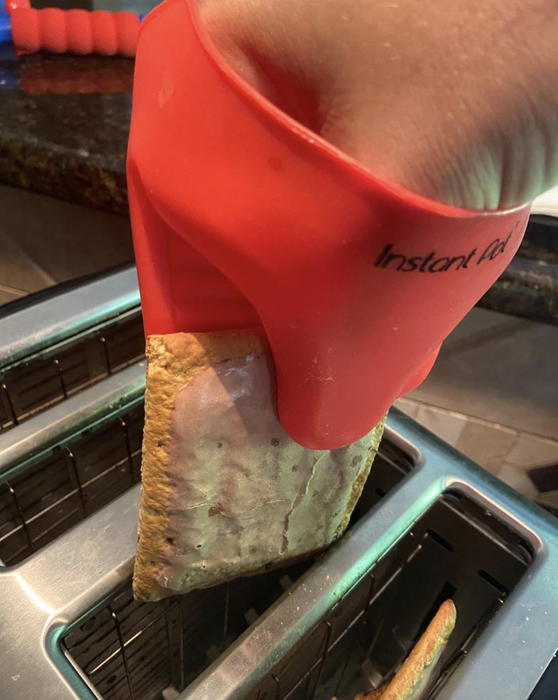 A reviewer demonstrates using the red oven mitt to safely retrieve toast from a toaster.
