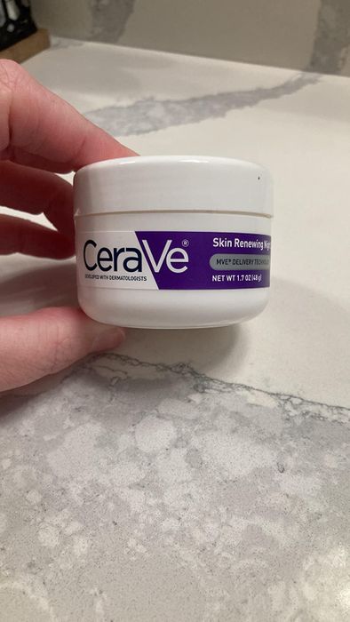reviewer holding a white and purple tub of moisturizer