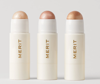 A trio of Merit Glow Highlighting Balm tubes, displaying the product's sleek packaging.