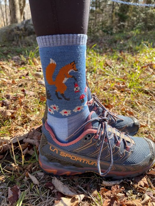 An outdoor scene with feet in hiking boots, paired with socks featuring foxes and mushrooms in the design