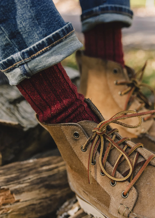 A person sporting rolled-up jeans, red socks, and tan suede boots with laces.