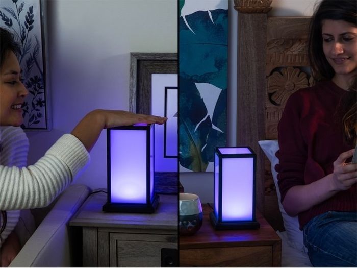 Split-screen image showing one person touching the lamp while the other watches theirs light up