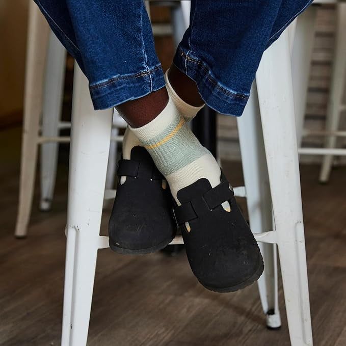 A person in jeans, wearing black slip-on shoes and beige socks, sitting comfortably on a tall stool