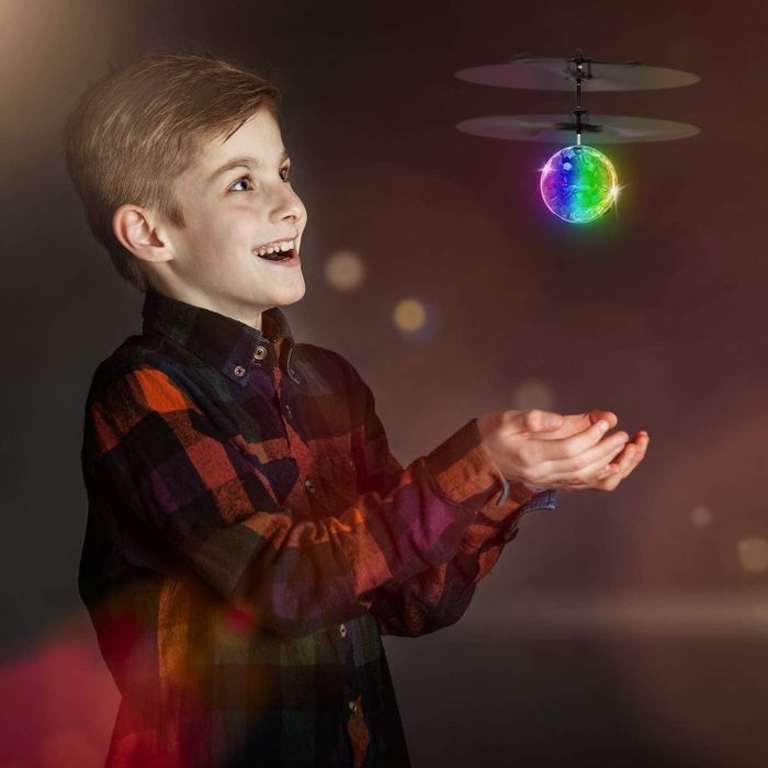 A child hovering their hand beneath the shiny, spherical disco drone