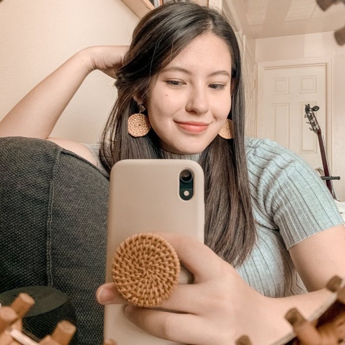 A person using the rattan phone stand to hold their phone