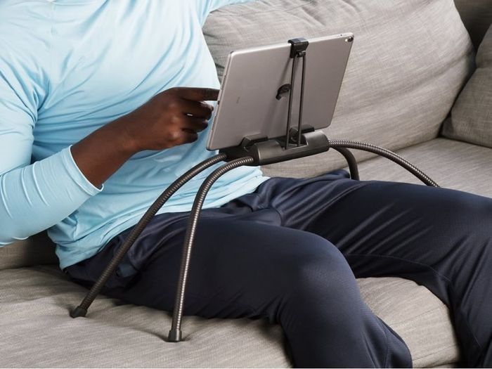 The black tablet holder with four legs, positioned over a model's legs, demonstrating how it effortlessly supports the tablet