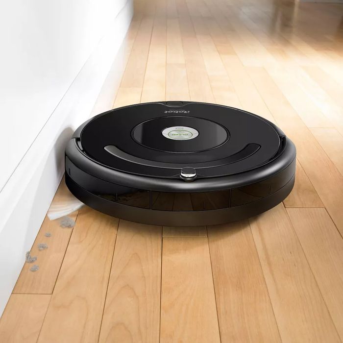 A black Roomba vacuum cleaning a hardwood floor.