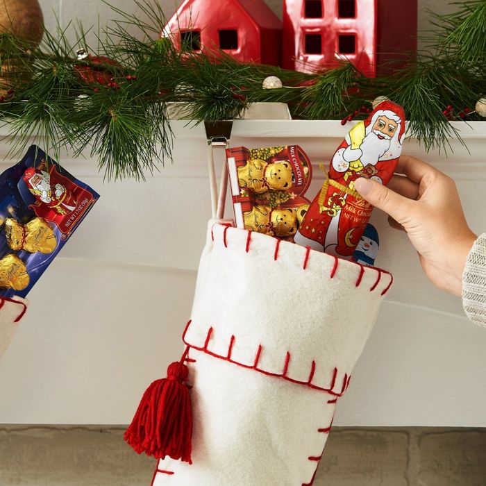 Stockings are filled with chocolate Santas and other festive confections, dangling from a mantel adorned with greenery and red houses