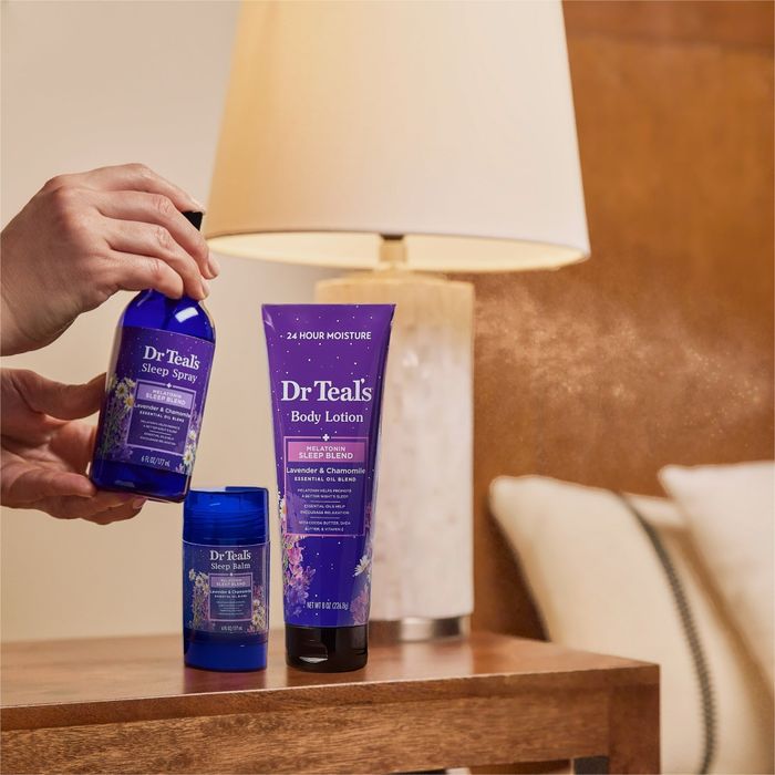 Dr. Teal's products, including a sleep spray and body lotion, are neatly arranged on a bedside table beside a cozy lamp.