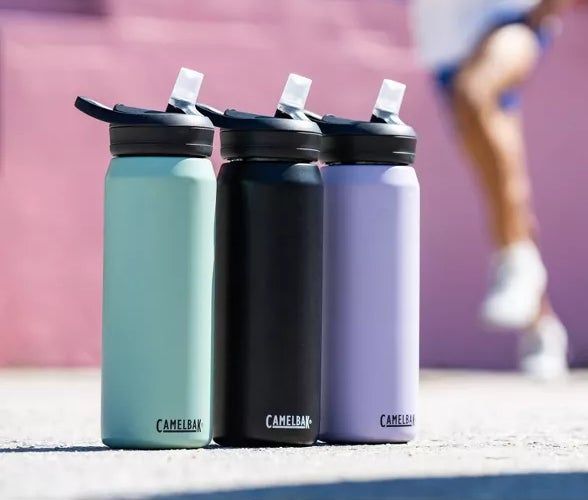 Two runners in blurred motion, dressed in activewear, are seen in the background, while three CamelBak water bottles are prominently displayed in the foreground, as featured in a shopping guide article.