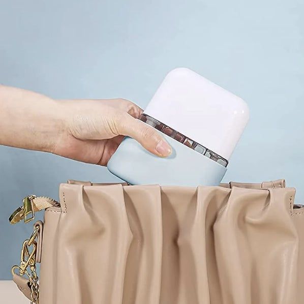 A hand gently places a compact, rectangular object into a beige handbag with a gold chain detail, capturing a stylish shopping moment.