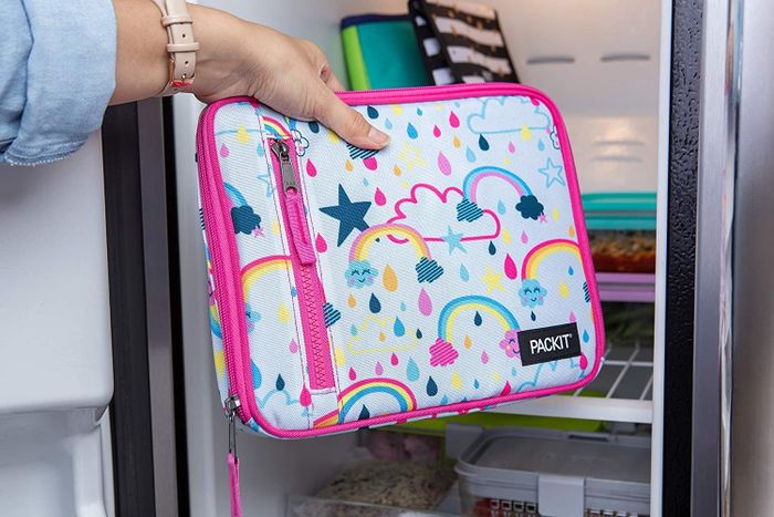 A model’s hand placing a bright pink, rainbow-themed lunch bag with trim into a fridge.