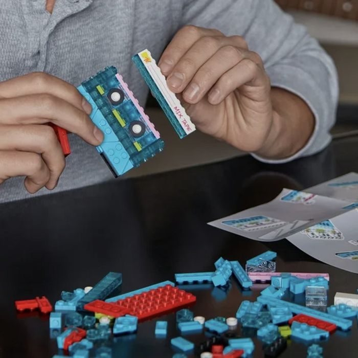 Hands piecing together a toy building kit with a cassette tape design, surrounded by instruction sheets and building blocks on a table.