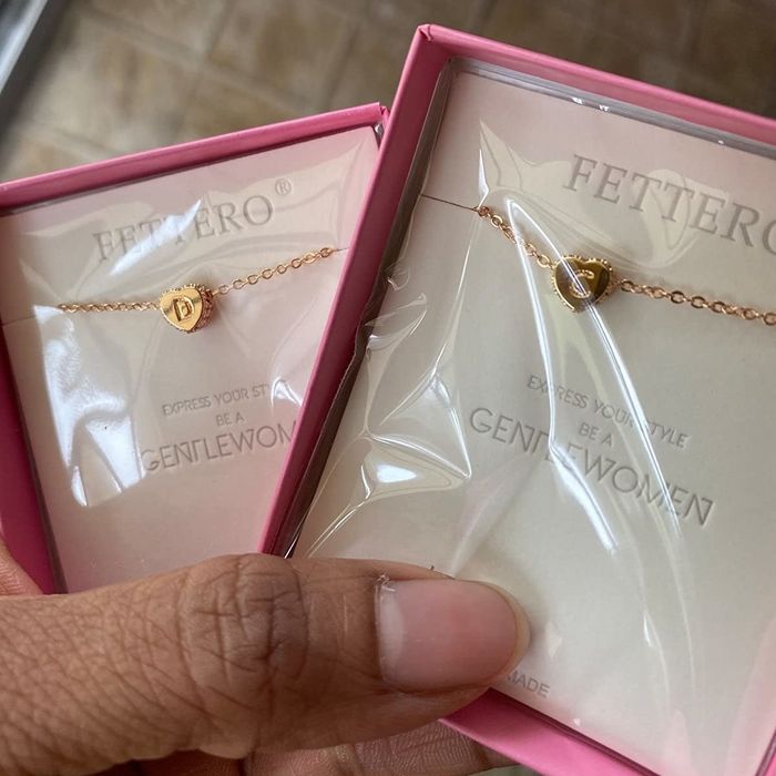 Reviewer holding two packaged heart-shaped necklaces with cubic zirconia detailing, featuring the initials 