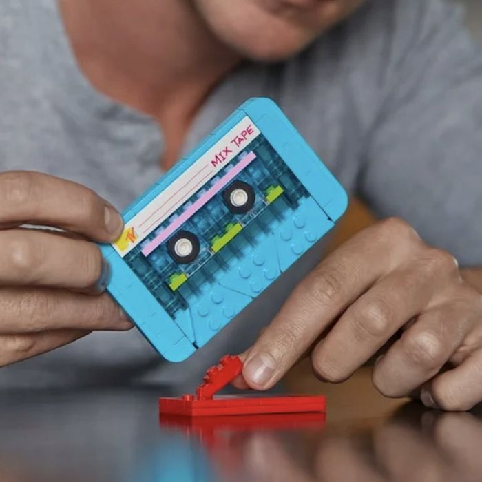 A person holding a LEGO cassette tape along with a mini stand, showcasing ideas for gifts inspired by retro tech and toys.