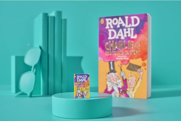 A photo showcasing the book 'Charlie and the Chocolate Factory' by Roald Dahl, displayed on a pedestal along with a miniature replica and decorative touches.