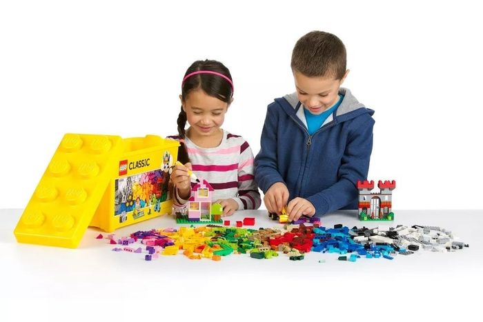 Two young children having fun playing with a table filled with vibrant Lego blocks.