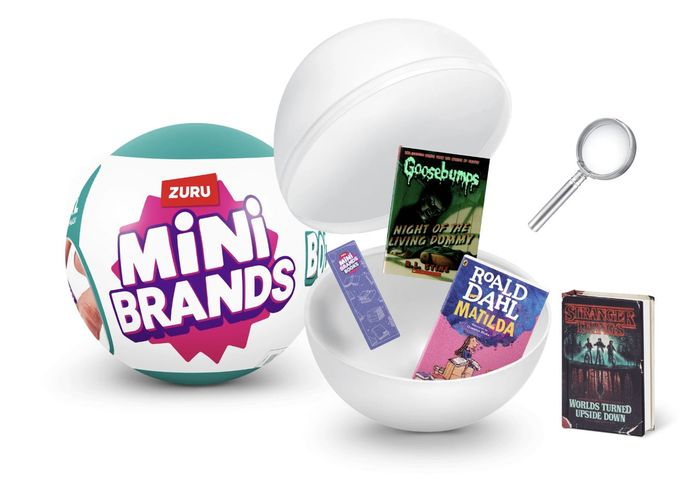 A Mini Brands toy capsule reveals tiny book replicas, such as Goosebumps and Matilda, with a magnifying glass for scale.