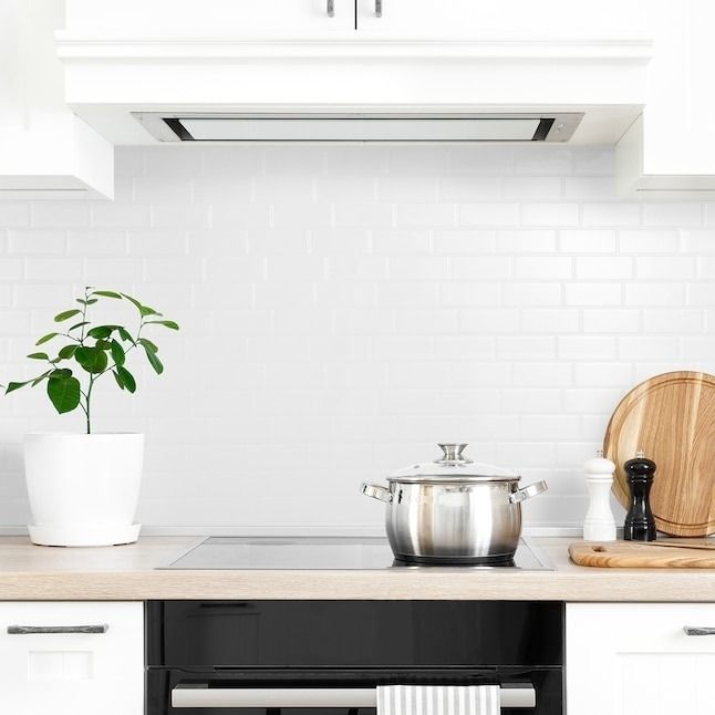 A contemporary kitchen featuring a stovetop, a pot, wooden cutting boards, and a potted plant on the counter, set against a white subway tile backsplash.