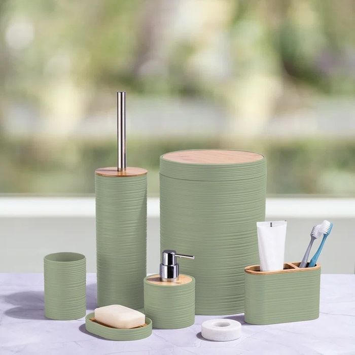 A bathroom accessory set featuring a toothbrush holder, soap dispenser, soap dish, toilet brush, and waste bin, all designed with bamboo accents.