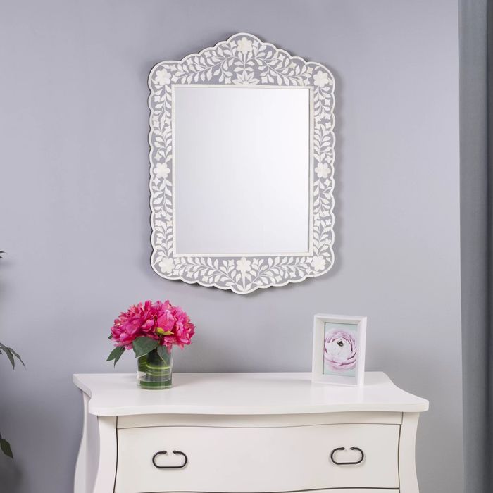 A white dresser with two drawers displays a framed flower photo and a vase of pink blooms. Above it, a decorative wall mirror is hung.