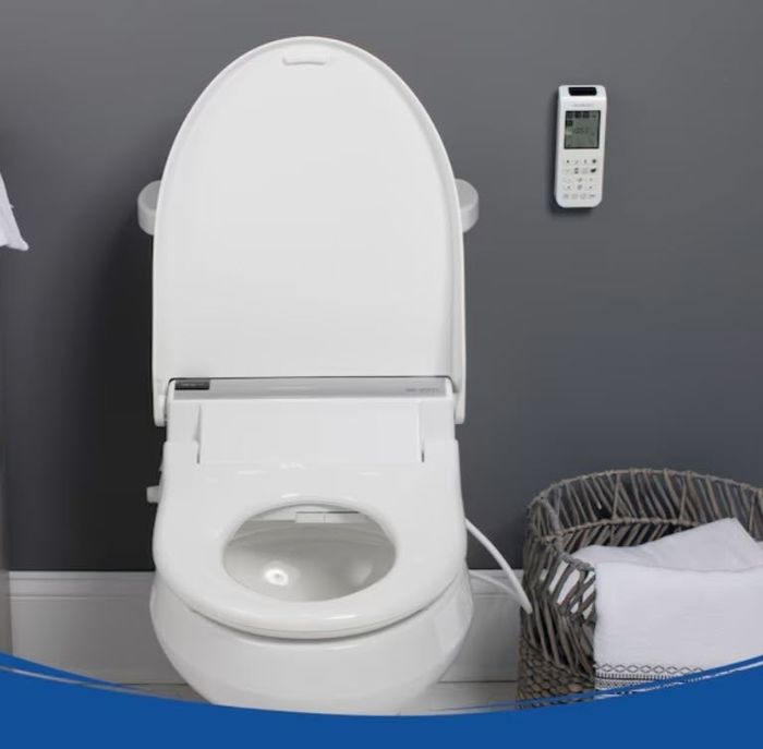 A contemporary bidet toilet featuring a remote control and a conveniently placed towel basket nearby.