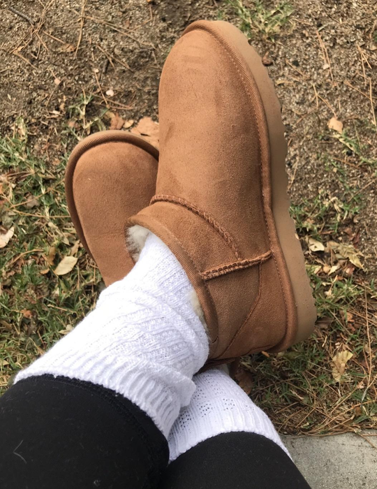 Close-up of a reviewer wearing brown Ugg boots, white socks, and black leggings, with a grassy and earthy background