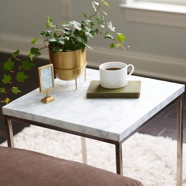 An elegant marble side table featuring a potted plant, a small photo frame, and a book accompanied by a coffee cup, all set on a plush rug