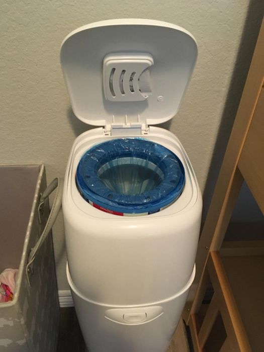 A white diaper pail with its lid open, revealing a blue bag liner inside.