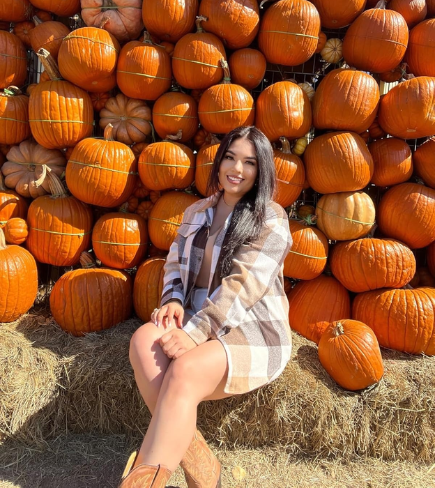 reviewer striking a pose in front of a pumpkin display, sporting a plaid coat and cowboy boots
