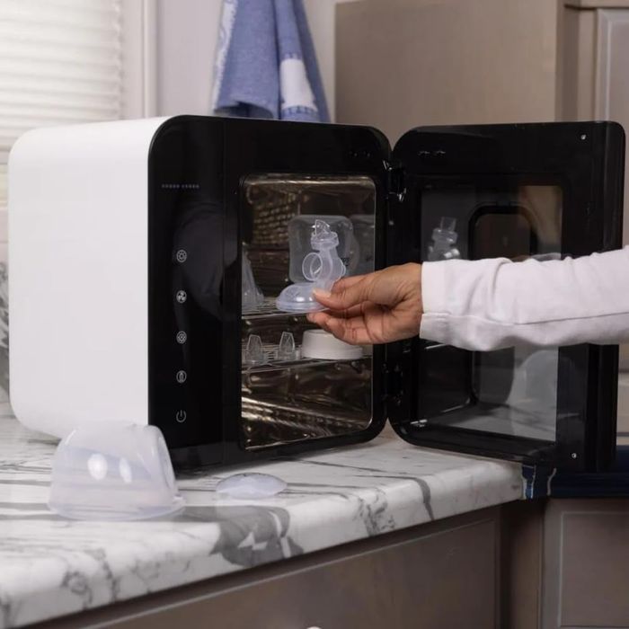 A person is placing a silicone lid inside a compact black and white sterilizer positioned on a kitchen counter.