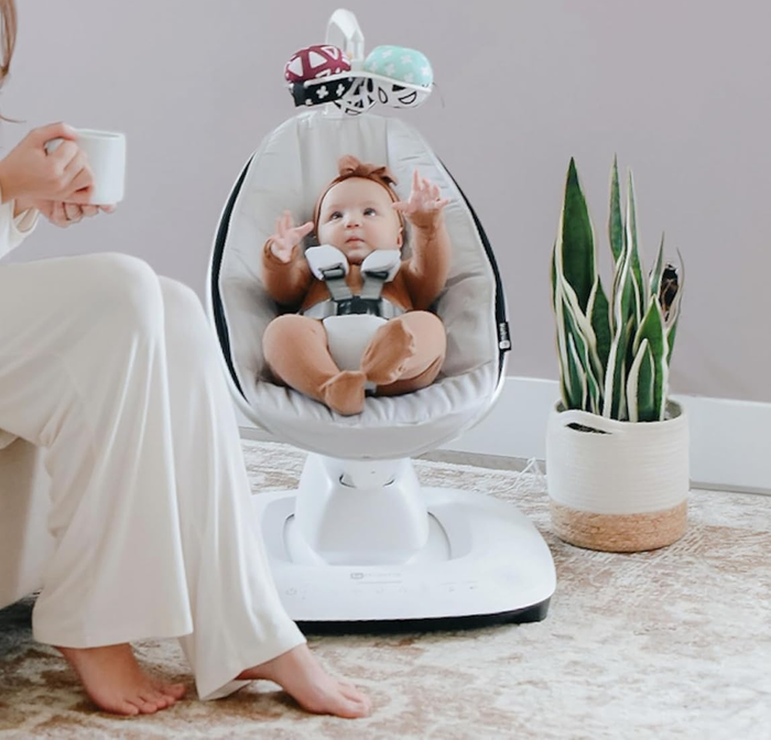 A baby comfortably seated in a modern white baby swing with advanced features.