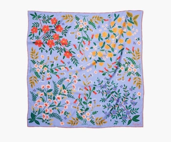 The beautiful periwinkle scarf adorned with red piping, featuring delicate illustrations of vibrant flowers in red, yellow, pink, and purple hues.