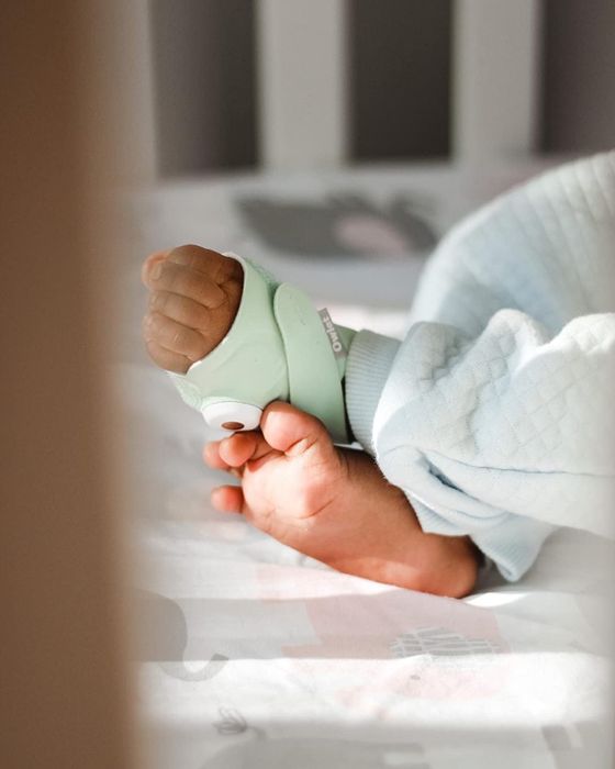 A baby wearing a wearable monitor on their foot, resting peacefully in a crib.